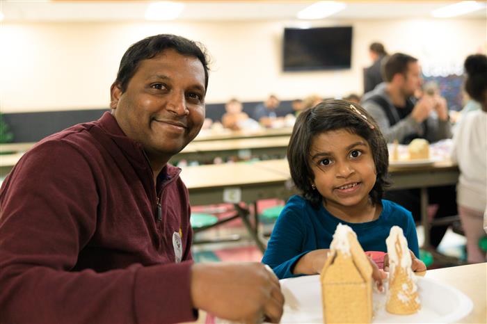 Father and daughter posing in front of their gingerbread house